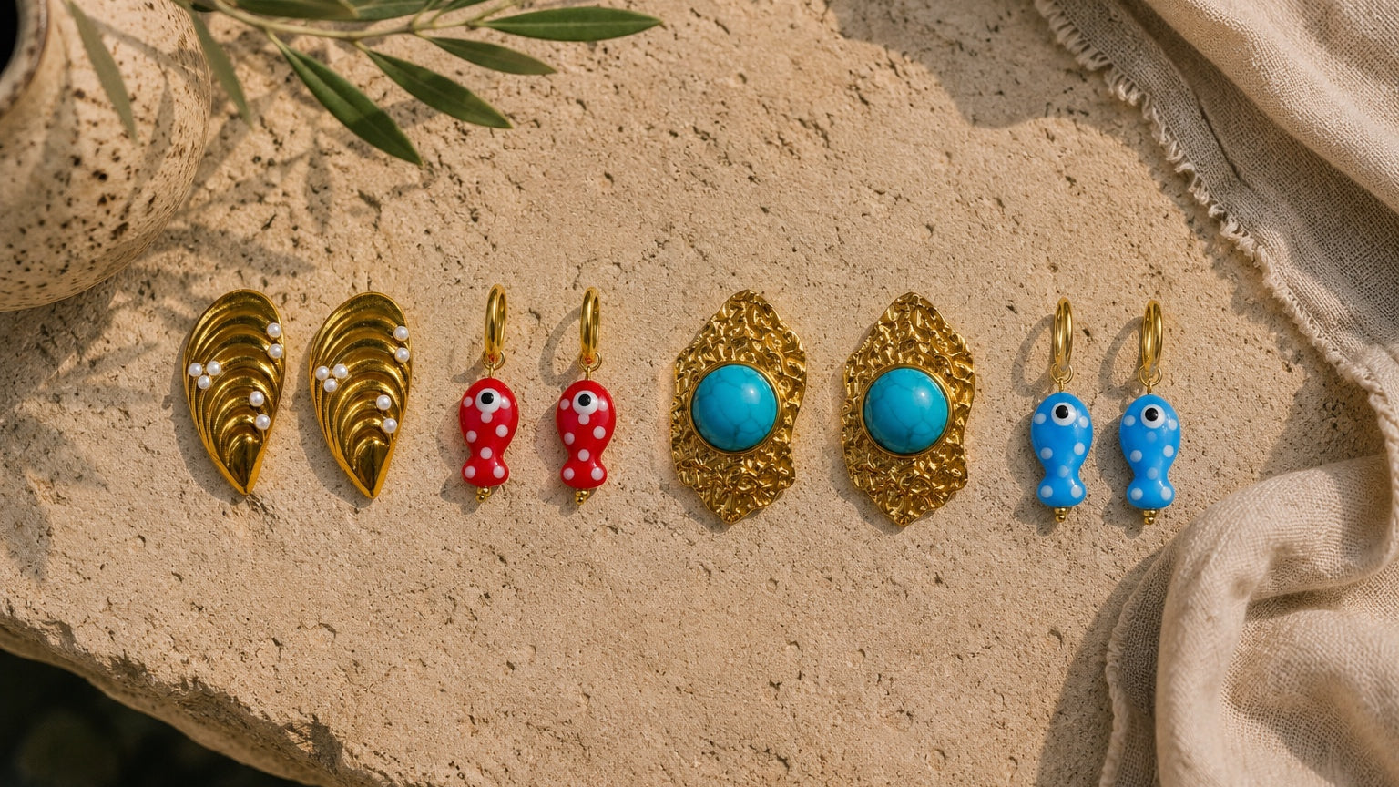 Set of earrings on a textured surface with leaves and fabric