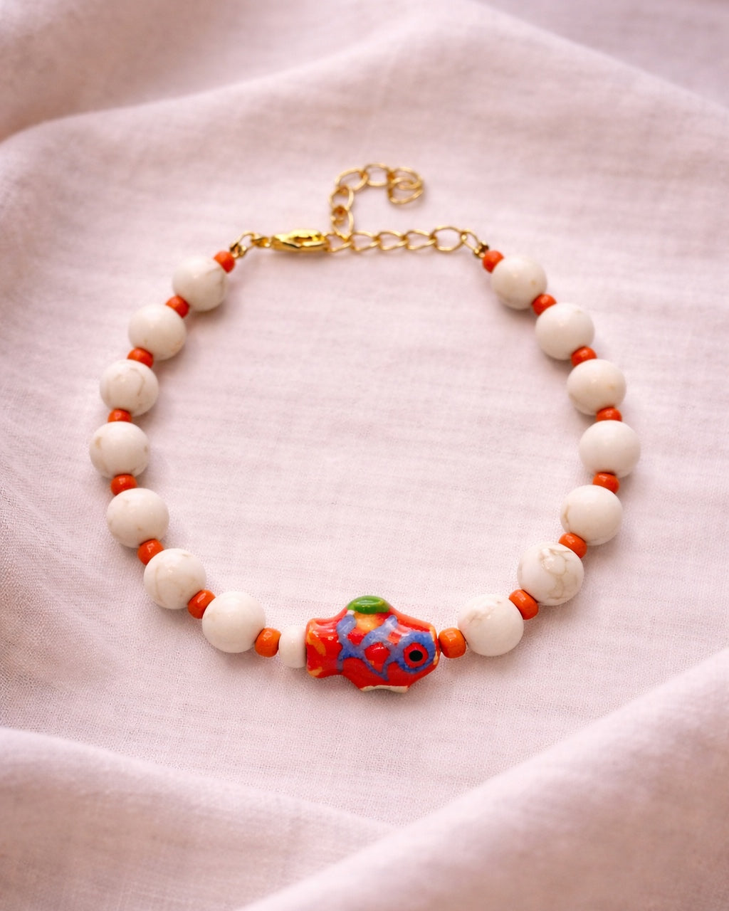 Elegant gold bracelet with ecru beads and ceramic fish charm, handmade jewelry inspired by the sea with natural coastal style