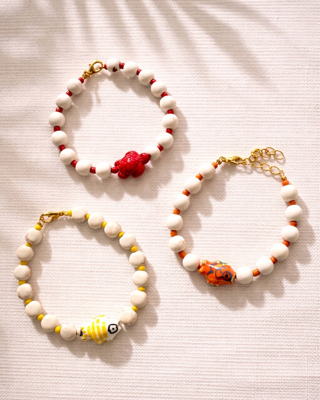 Elegant gold bracelet with ecru beads and fish charm, minimalist handmade jewelry inspired by the sea and coastal style