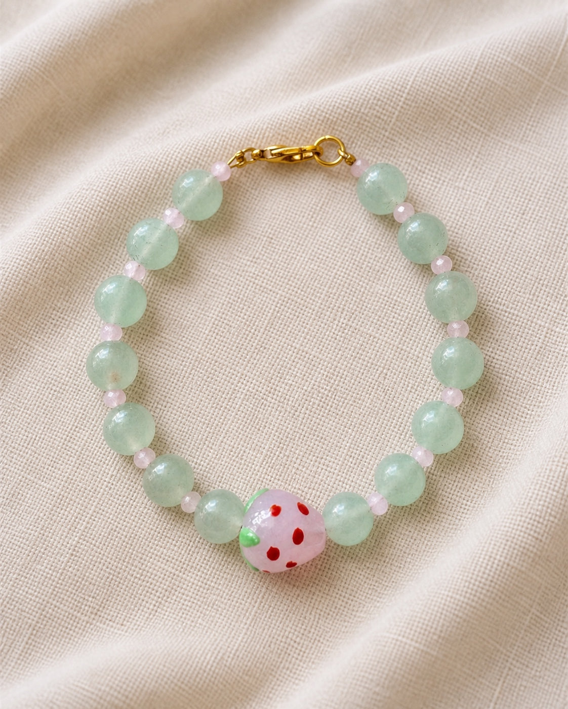 Gold bracelet with green beads and strawberry charm.