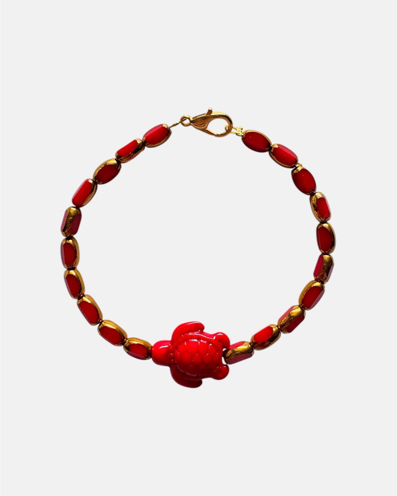 Elegant gold bracelet with red glass beads and ceramic turtle charm, stylish handmade jewelry inspired by nature and coastal design
