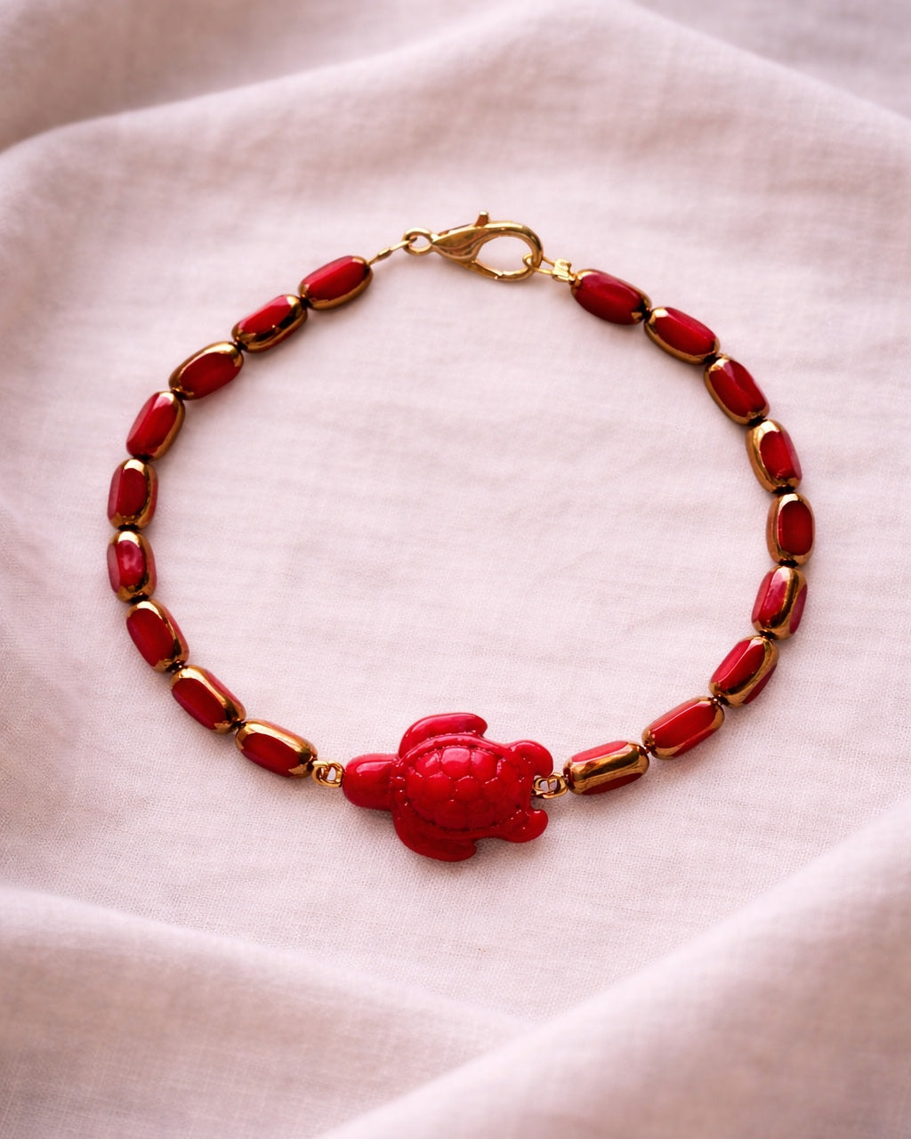 Elegant gold bracelet with red glass beads and ceramic turtle charm, stylish handmade jewelry inspired by nature and coastal design