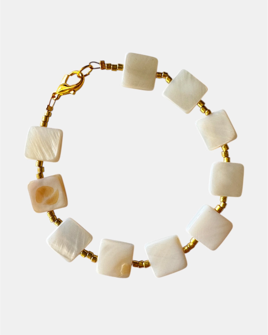 Bracelet with gold accents and white square beads on a white background