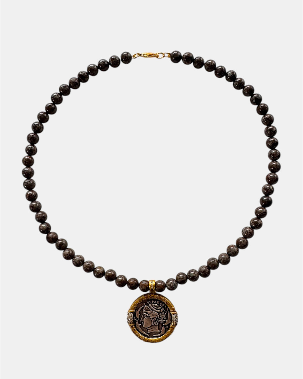 Necklace with dark beads and a gold coin pendant on a white background