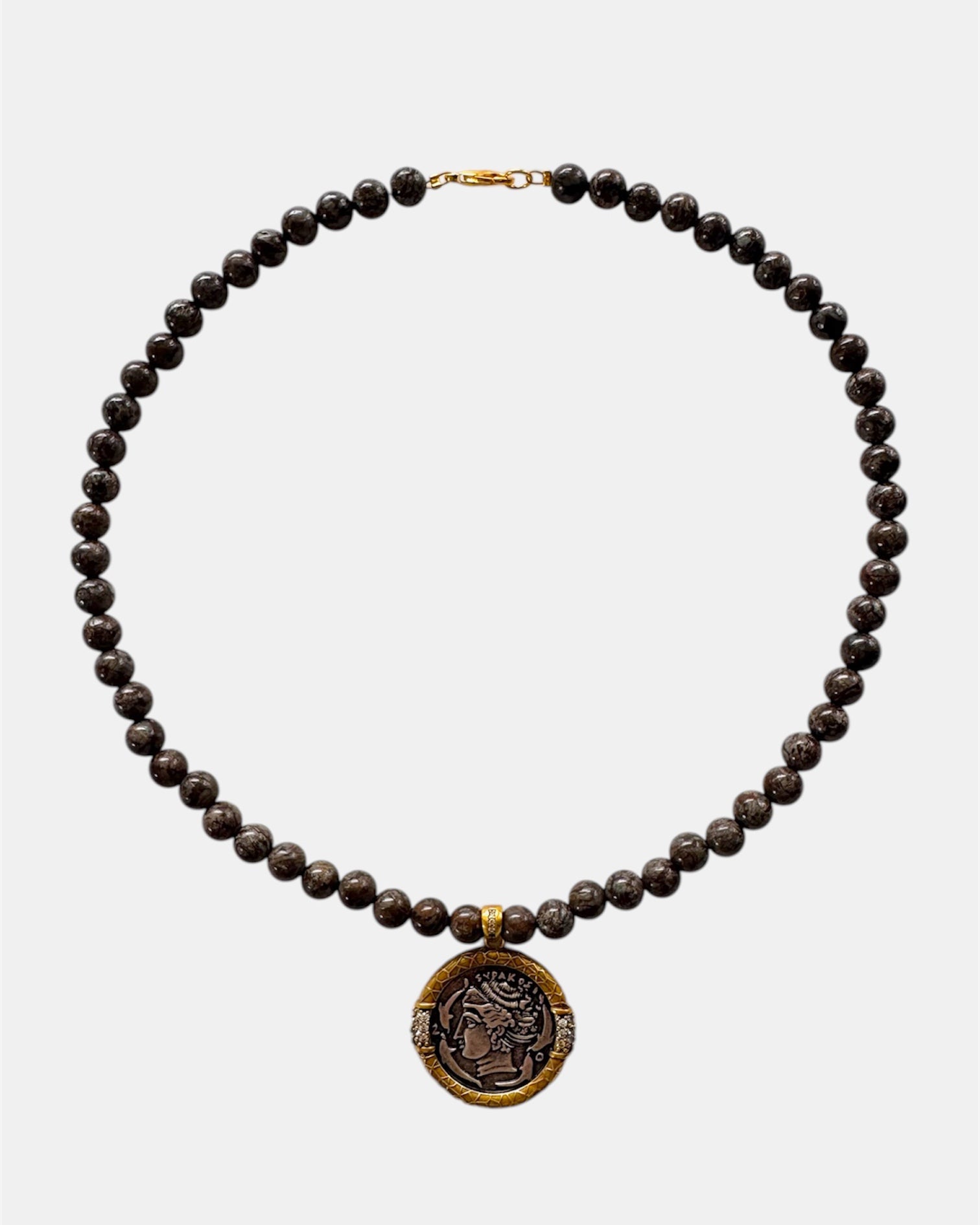 Necklace with dark beads and a gold coin pendant on a white background