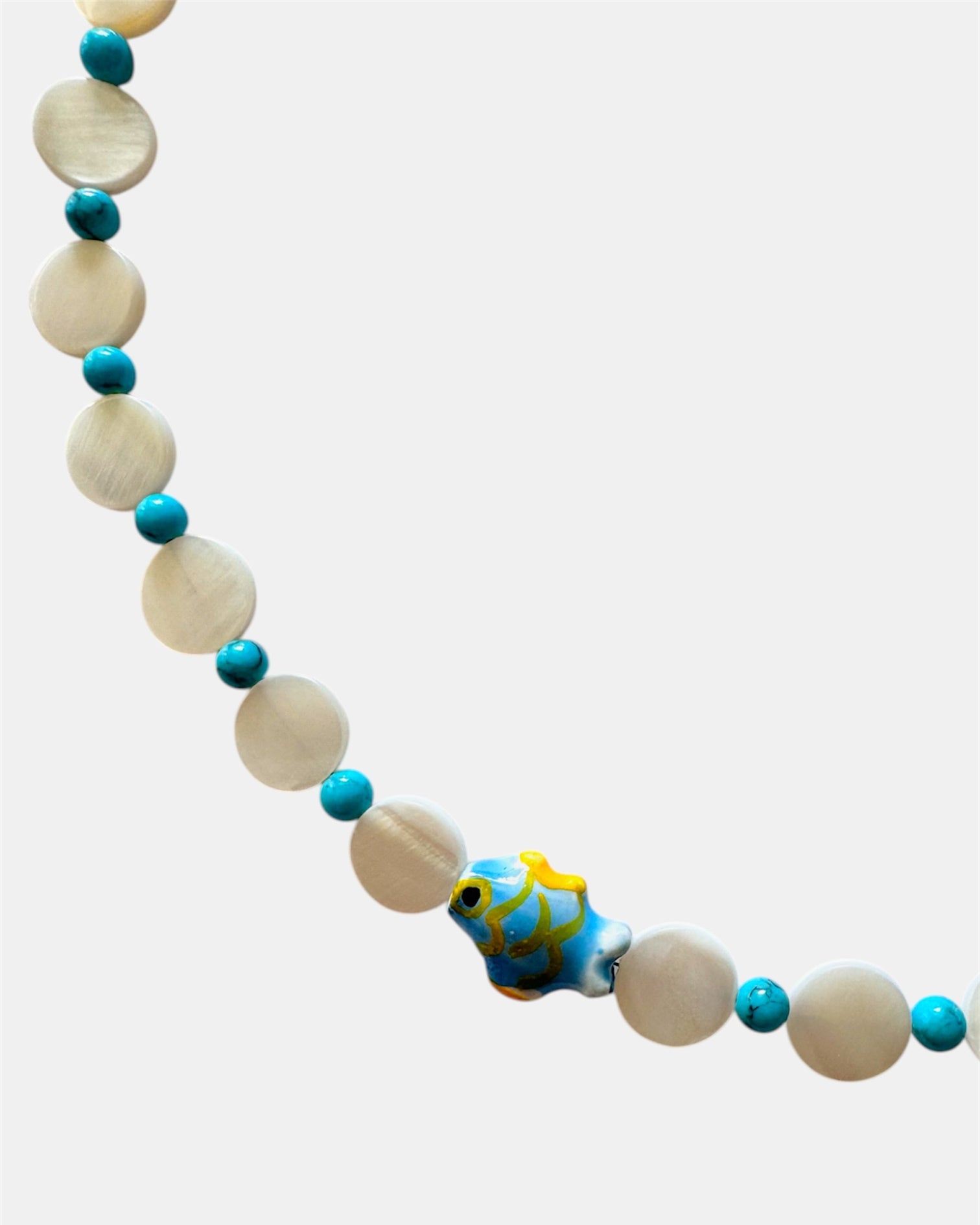 Necklace with white beads and blue accents featuring a fish-shaped charm on a white background