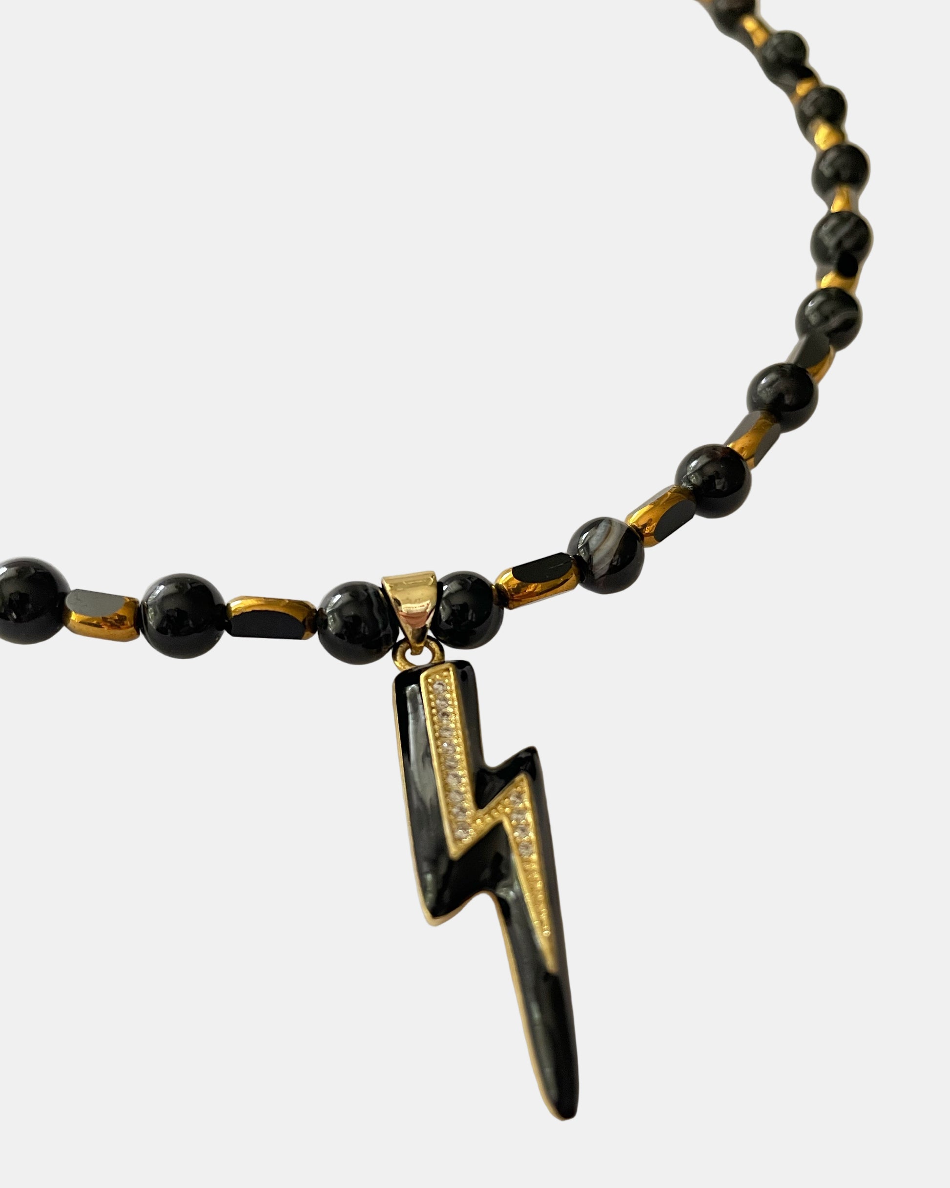 Χειροποίητο μαύρο κολιέ με χρυσές λεπτομέρειες και κεντρικό μεταλλικό στοιχείο αστραπής.