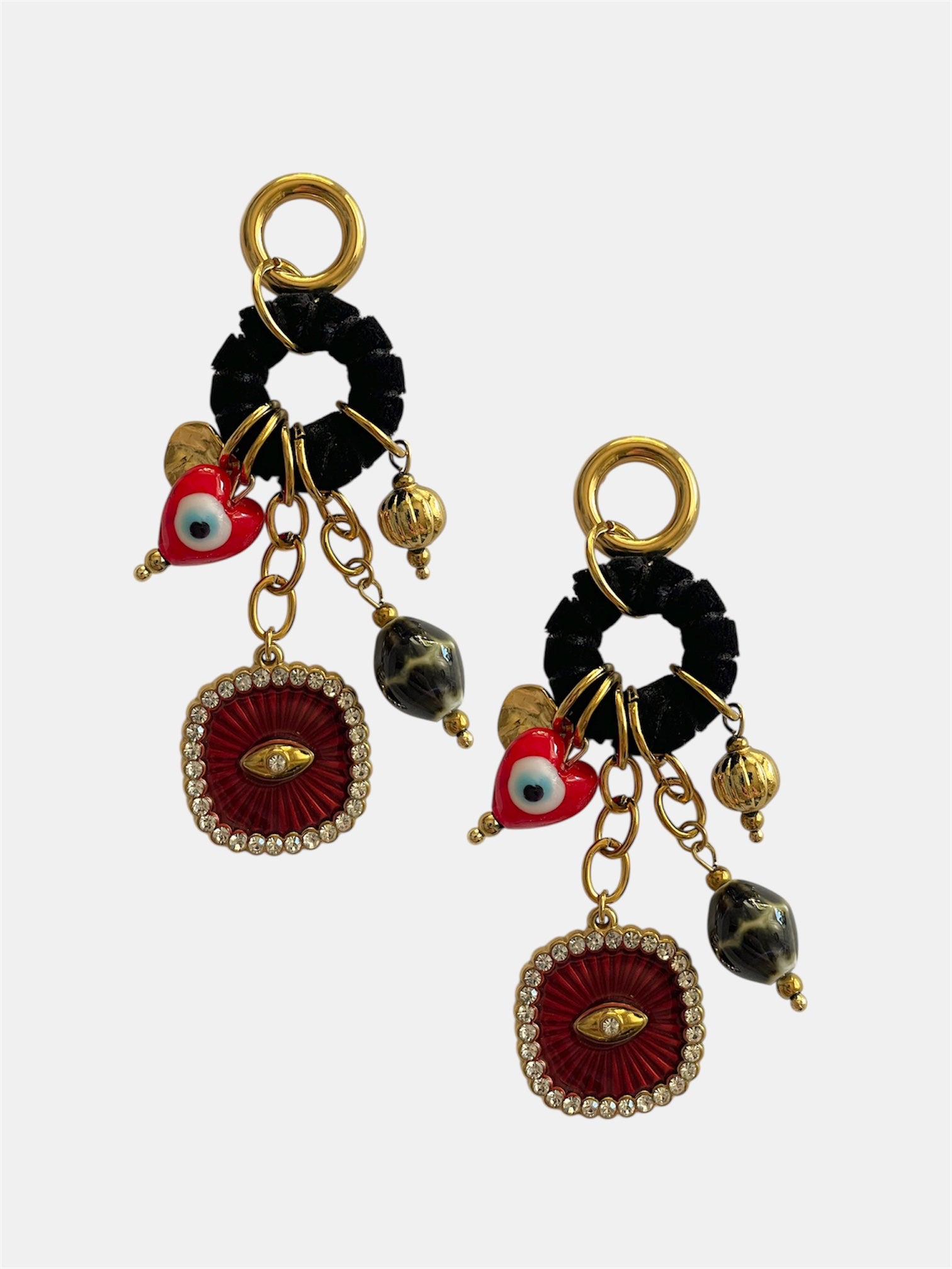 Ζευγάρι εντυπωσιακών κρεμαστών σκουλαρικιών με χρυσές λεπτομέρειες, μαύρο υφασμάτινο κρίκο και κρεμαστά charms, όπως κόκκινη καρδιά με μάτι, μαρμαριζέ χάντρα και κεντρικό κόκκινο μοτίφ με στρας. Το σύνολο δημιουργεί μια boho–artistic αισθητική με έντονο χαρακτήρα και λάμψη.
